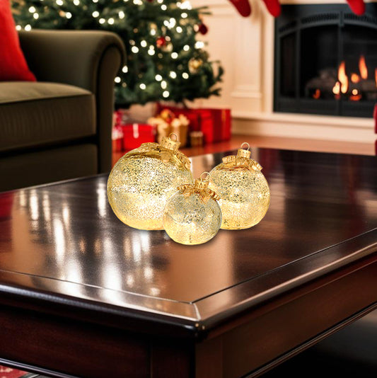 Decorative gold mercury glass ornaments on a coffee table with a Christmas tree and fireplace in the background.