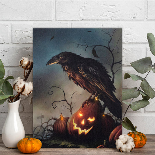 Framed artwork of a crow perched on a pumpkin with glowing eyes, surrounded by pumpkins and cotton on a wooden surface.