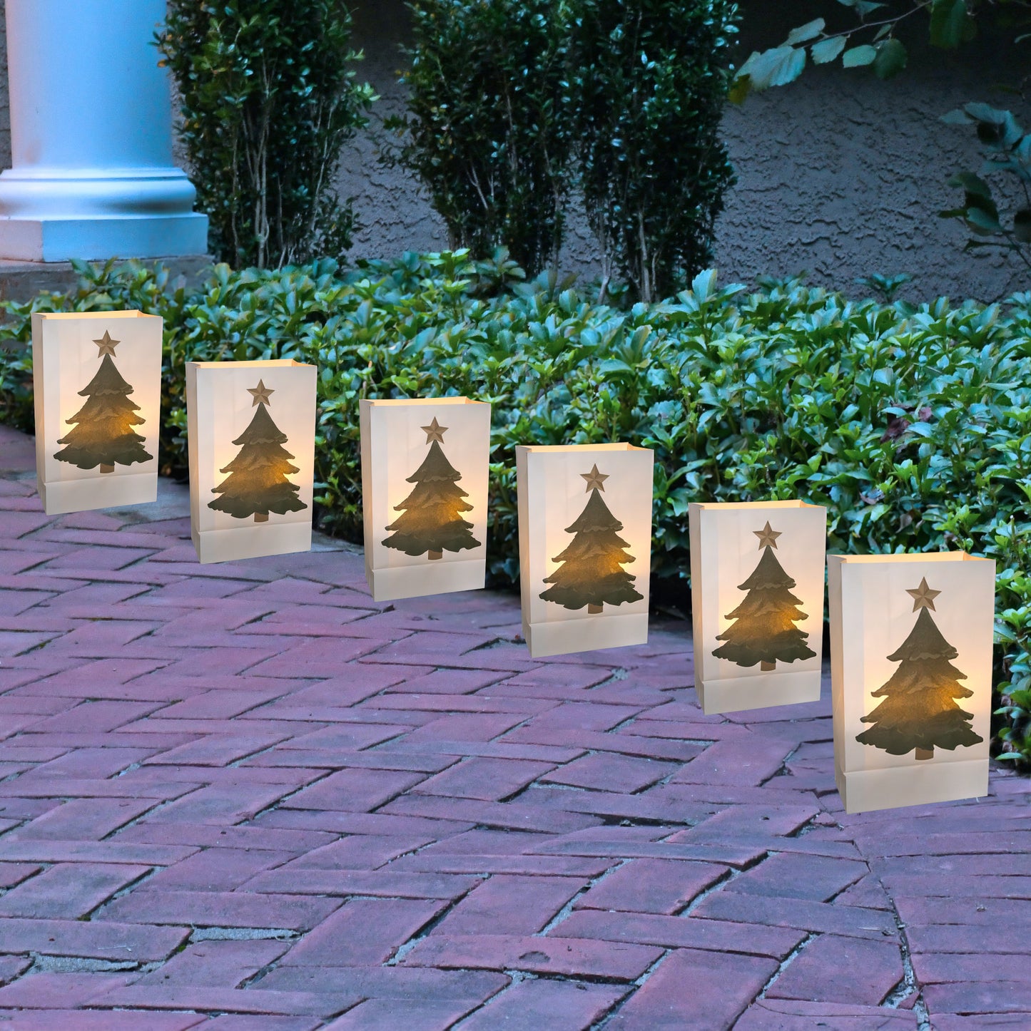 Set of six Christmas tree-themed luminaries on a brick patio