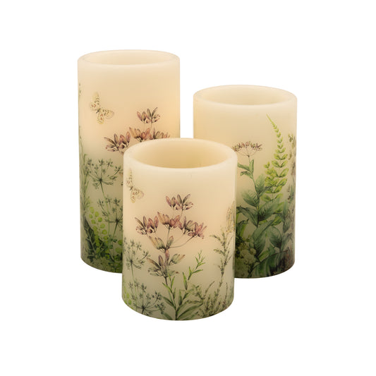 A set of three white wax candles with floral designs and greenery motifs, featuring an amber flickering LED light.
