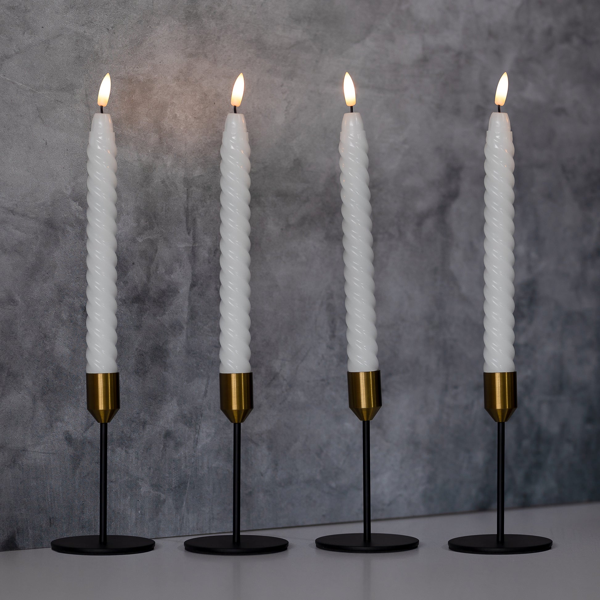 Set of four battery operated  flameless twisted wax taper candles with 3D wick in candleholders on shelf.