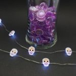 Halloween fairy lights battery operated sugar skull lights in front of vase with purple rocks.