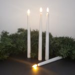 Battery Operated Taper Candles with Remote Control, set of 4, on a black table with garland.
