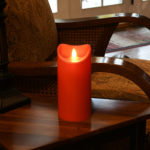 Red battery operated pillar candle on nightstand.